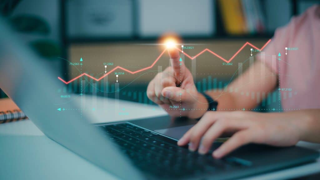 Woman at work on a laptop computer and pointing at a datapoint on a data visualisation graph which is imposed on the image.