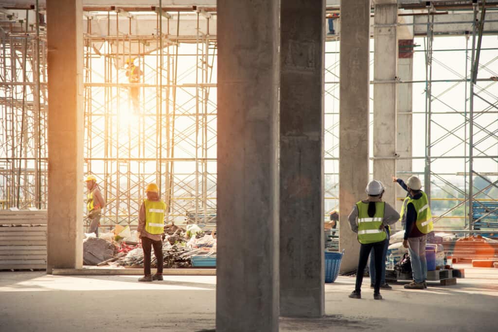 Construction engineers and other trades people and project managers on a large scale construction site with scaffolding and exposed concrete pillars.