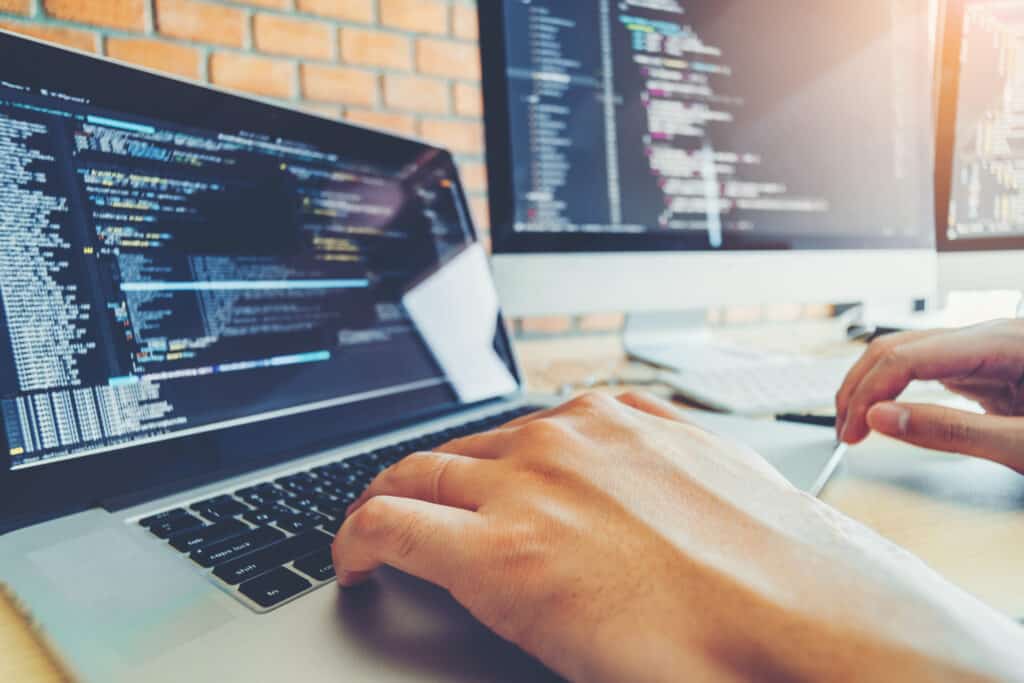 Hands of a software developer working on code on a laptop and desktop computer