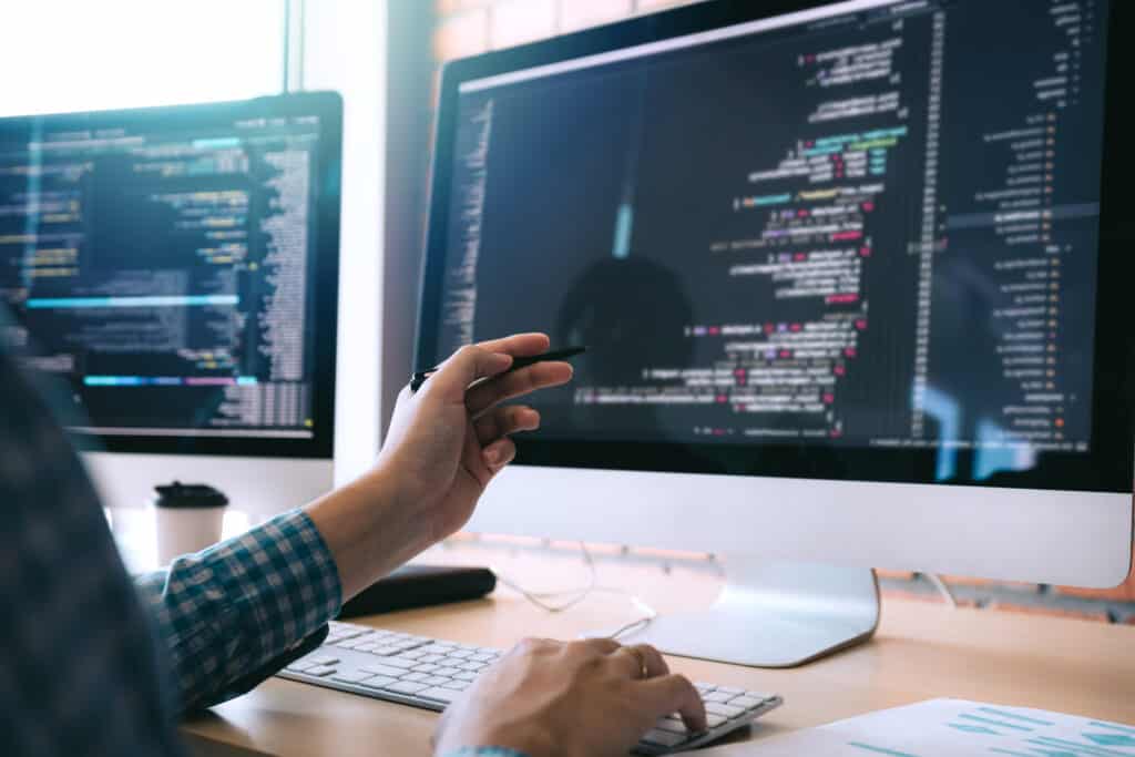 Software developer holds a pen pointing to the computer screen full of code.